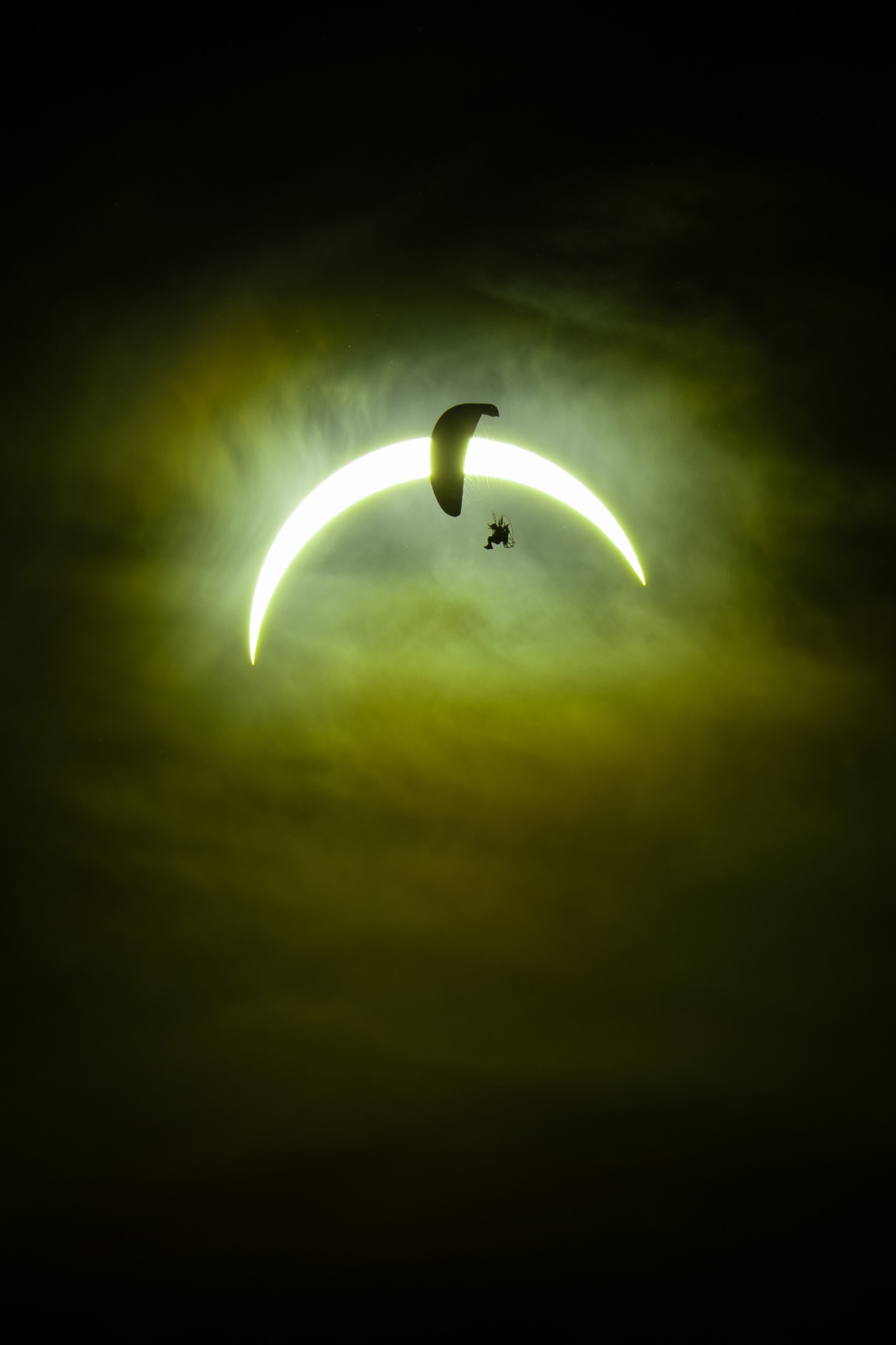 A paramotor pilot flies in front of a partial solar eclipse